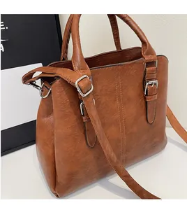 Detail of caramel brown faux leather handbag with adjustable strap and silver metal buckles
