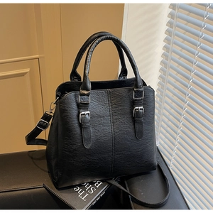 Detail shot of black textured faux leather handbag with silver metal buckle and top handles