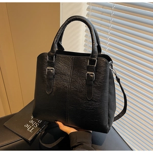 Detail of black lychee grain leather handbag with silver buckles and curved handles