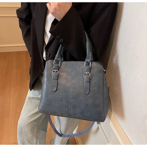 Close-up of blue-gray textured leather tote featuring silver metal buckles and handles
