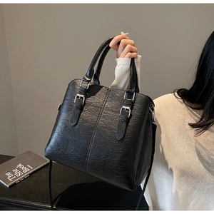 Close-up of black litchi pattern leather handbag with silver buckles and fine stitching