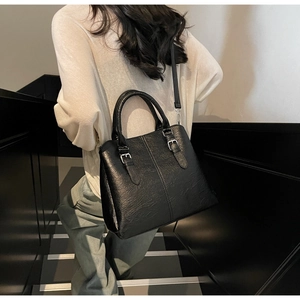 Side view of black faux leather handbag with shoulder strap on female model in minimalist setting
