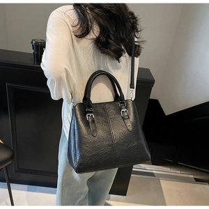 Close-up of black textured leather handbag with silver buckles on a casual model