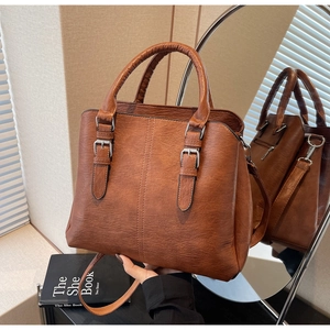 Detail of caramel tote bag with double handles, textured leather, and buckle accents