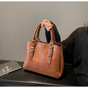 Detail of a brown leather tote bag with lychee texture and silver buckle accents