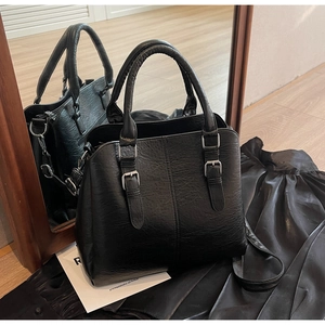 Detail of black pebbled leather tote bag with silver buckles on a satin background