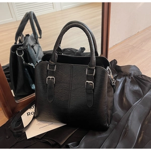 Detail of a vintage black PU leather tote bag with silver buckles on a silk background