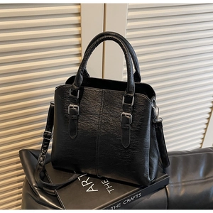 Detail of black textured leather handbag with silver buckles on a decorative book