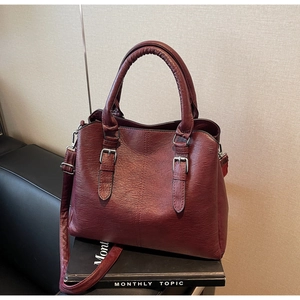 Detailed shot of dark red vintage faux leather handbag with silver buckles on a magazine