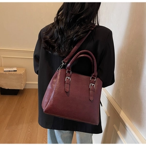 Deep red vintage tote bag with buckle details shown on a model in a warm interior