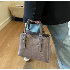 Macro detail of a grey pebbled leather tote bag with silver buckles and a top handle