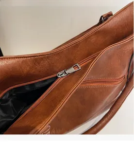 Close-up of caramel brown leather tote bag showing silver metal zipper and smooth closure
