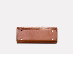 Detail view of brown crocodile-embossed leather tote bag bottom with silver protective feet