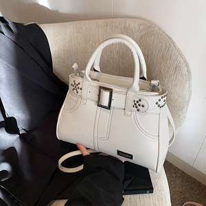 Sac à main blanc avec rivets, boucles métalliques et bandoulière sur un canapé