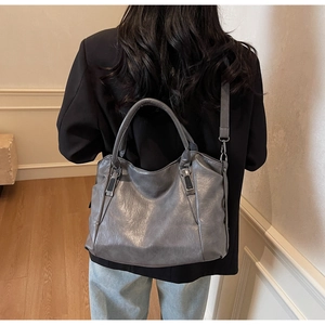 Detailed back view of a grey leather tote bag worn by a model in a minimalist room