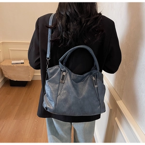 Model wearing a large dark blue tote bag with adjustable strap and textured finish