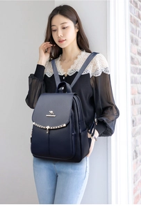 Detail of navy blue pebble leather backpack featuring metal kangaroo logo and chain decor