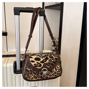 Detail of leopard print shoulder bag with brown leather trim hanging on luggage