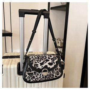 Detailed close-up of leopard print shoulder bag with silver round metal buckle on suitcase