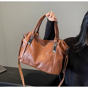 Detailed close-up of brown textured leather tote bag with metal buckles and soft handles