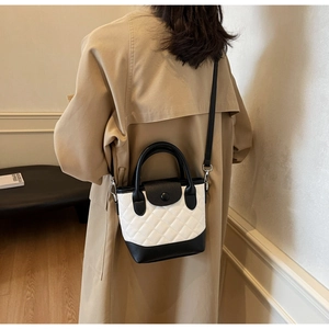 Dettaglio di una borsa a secchiello trapuntata bianca e nera su una modella in trench kaki