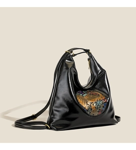 Detail of black glossy hobo bag featuring an ornate colorful metallic relief ornament