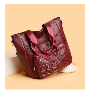 Detail of burgundy tote bag showing multiple zipper pockets and woven textile strap