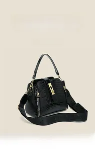 Detailed view of black crocodile pattern handbag with wide logo strap and gold hardware