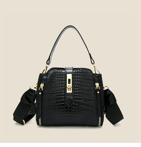 Detail of black faux crocodile patent leather handbag with gold clasp and wide strap