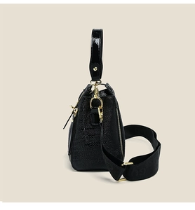 Detail of black crocodile texture handbag with gold metal hardware and wide strap