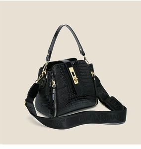 Detail of black faux crocodile patent leather bag with gold buckle and wide fabric strap