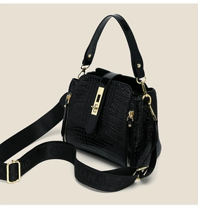 Detail of black patent croc-effect handbag with gold buckle and wide fabric strap