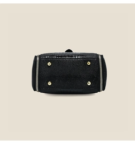 Detail view of black patent leather bag with stone pattern and gold metal feet on bottom