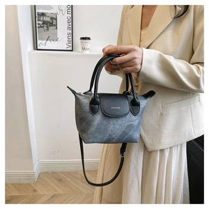 Détail d'un sac cabas en denim gris avec anses en cuir noir et bandoulière