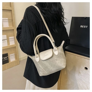 Détail d'un mini sac bandoulière en daim gris et cuir blanc porté par un mannequin