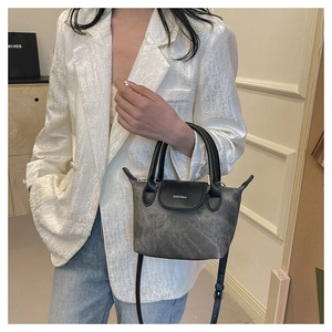 Détail du mini sac seau en daim gris avec poignées en cuir noir et bandoulière réglable