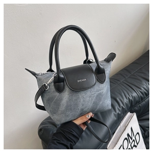 Détail du sac seau en denim gris avec poignée en cuir noir et logo ZHCNMA sur canapé