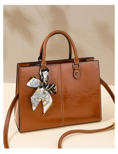 Detailed close-up of brown faux leather tote bag with white contrast stitching and silk scarf