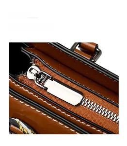 Detail of silver zipper and white stitching on brown leather handbag with silk scarf
