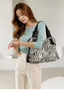 Detail of zebra print tote bag featuring black leather handles and silver metal studs