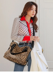 Leopard print tote bag with black handles and shoulder strap shown in a lifestyle setting