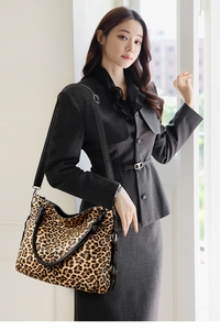 Detailed view of large leopard print tote bag with black leather straps on a model