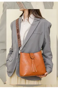 Détail du sac seau en cuir orange avec franges et large bandoulière à logo