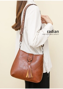 Détail d'un sac cabas en cuir marron avec pompon et large bandoulière en jacquard