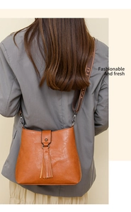 Détail d'un sac seau marron avec gland et large bandoulière tissée sur le modèle