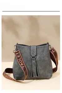 Détail d'un sac seau en cuir gris avec franges et large bandoulière à logo