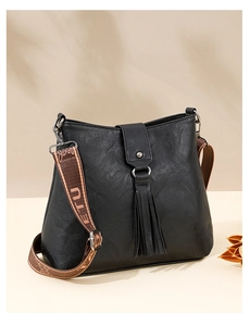 Détail du sac seau noir en cuir texturé litchi avec pompon et large bandoulière imprimée