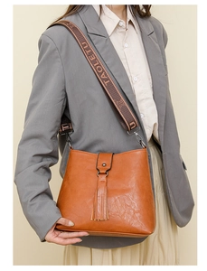Détail du sac seau marron orangé avec pompons à franges et bandoulière tissée logotypée