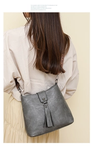 Détail d'un sac seau gris avec franges et large bandoulière en tissu avec lettrage