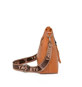 Détail de sac seau marron en cuir avec pompon et bandoulière large en tissu brodé
